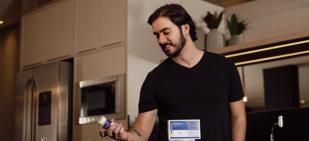 Man in a modern kitchen holding a vitamin supplement bottle, surrounded by health products.