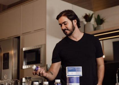 Man in a modern kitchen holding a vitamin supplement bottle, surrounded by health products.